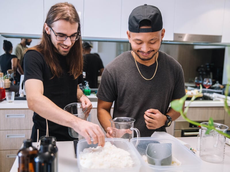 Two smiling men making candles in a kitchen